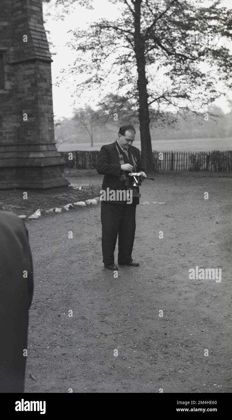 1950er, historisch, vor einer Kirche, ein Hochzeitsfotograf, der einen neuen Film in seine Kamera einbringt, England, Großbritannien. Stockfoto
