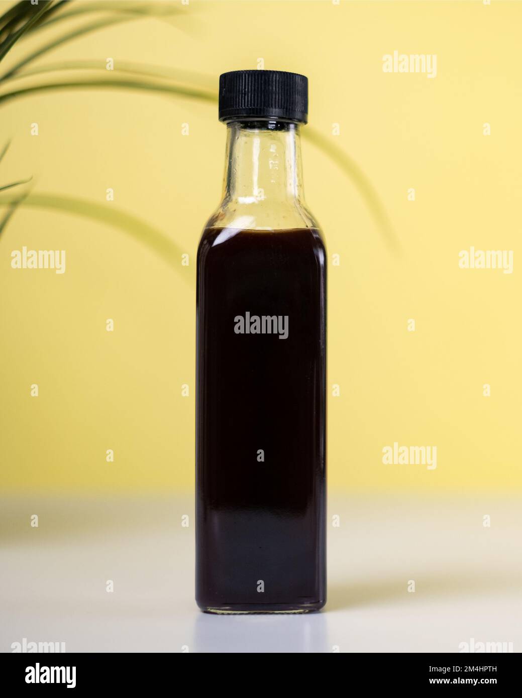 Vertikale Ansicht, Vollglasflasche mit gelbem Hintergrund. Nahaufnahme einer Glasflasche im Studio. Stockfoto
