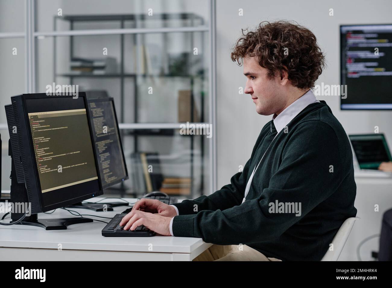 Junger IT-Spezialist, der Programmcodes auf dem Computer schreibt, während er an seinem Arbeitsplatz im IT-Büro sitzt Stockfoto
