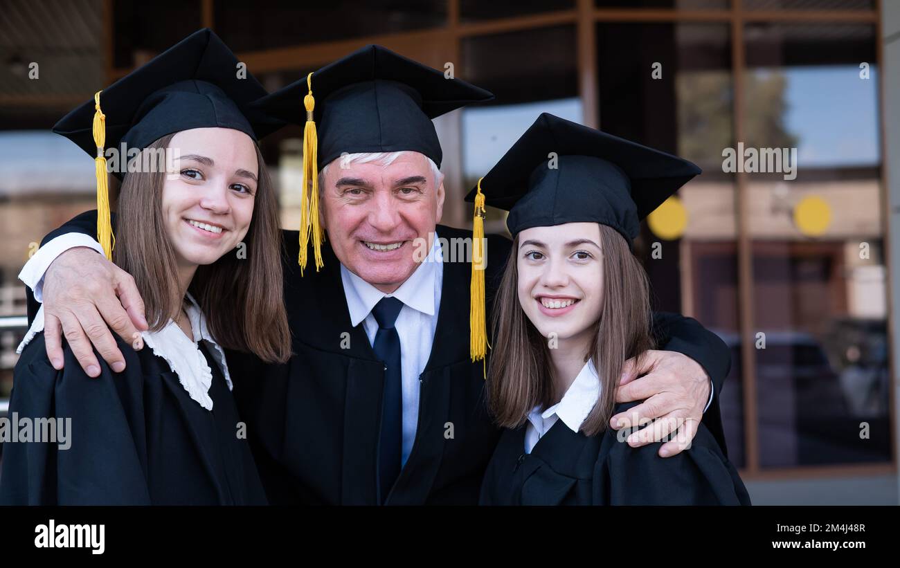 Professor umarmt Studentinnen in Abschlusskleidern. Stockfoto