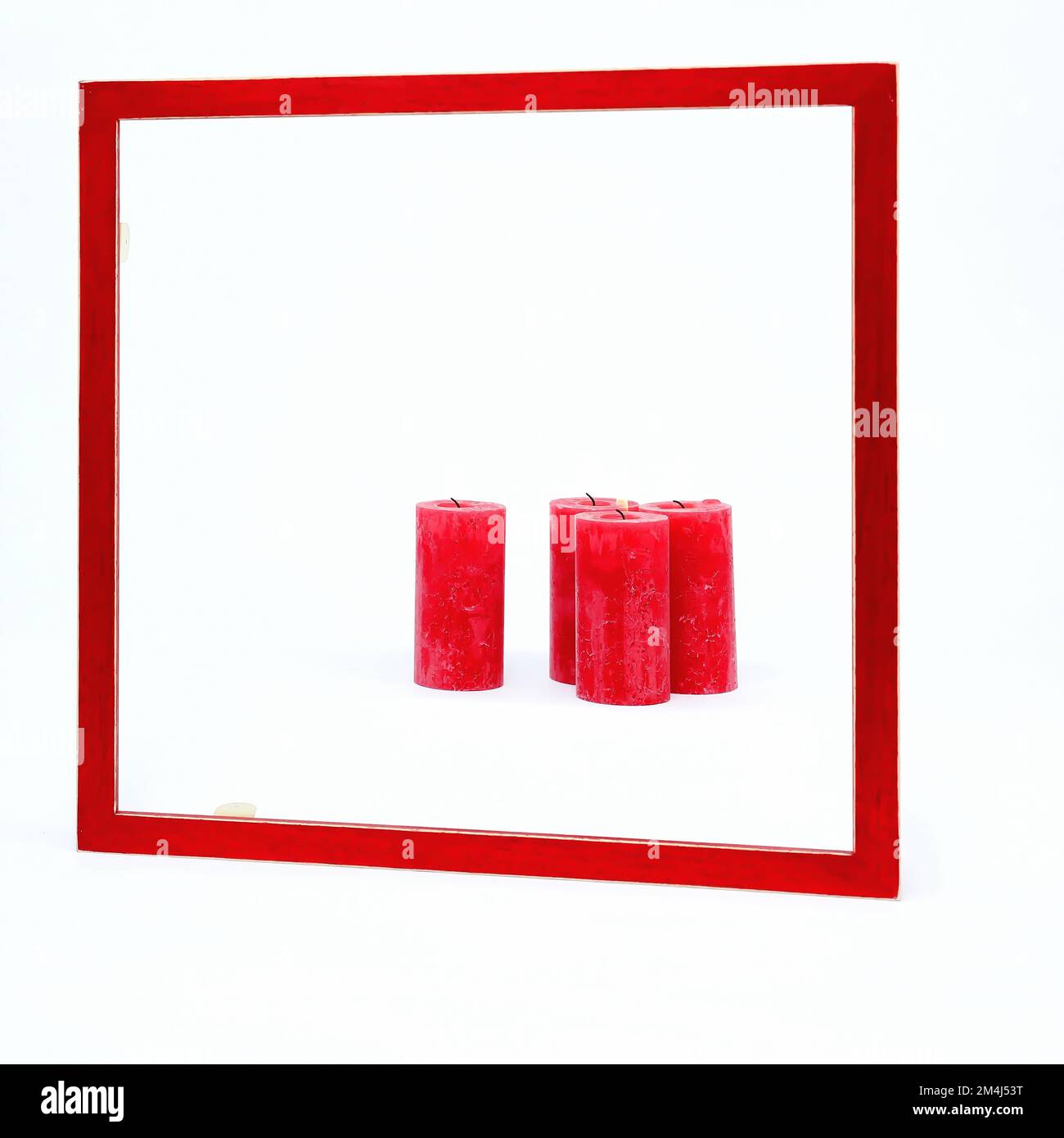 Quadratischer roter Rahmen auf weißem Hintergrund. Vier rote Kerzen sind im Rahmen. Eine Kerze brennt Stockfoto