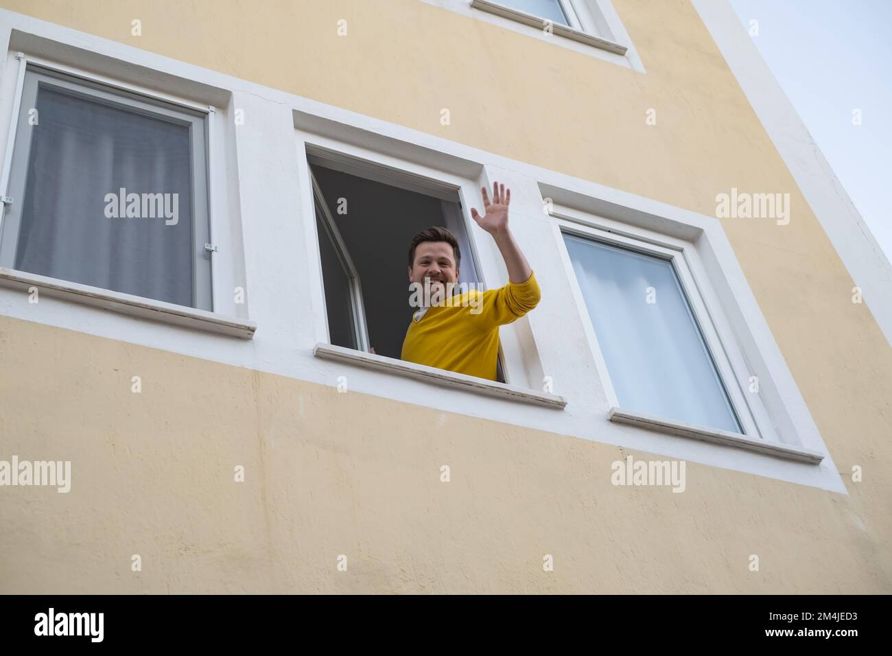 Ein erwachsener Mann winkte mit der Hand und begrüßte seinen Freund vom Fenster aus. Stockfoto