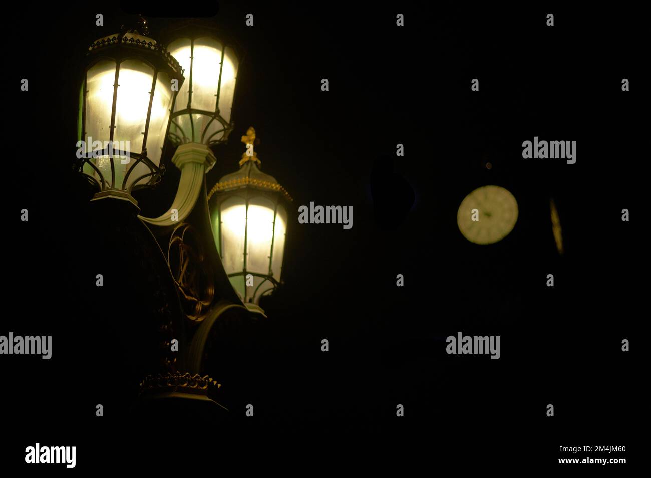 Straßenbeleuchtung im alten Stil mit verschwommener Uhr im Hintergrund bei Nacht Stockfoto