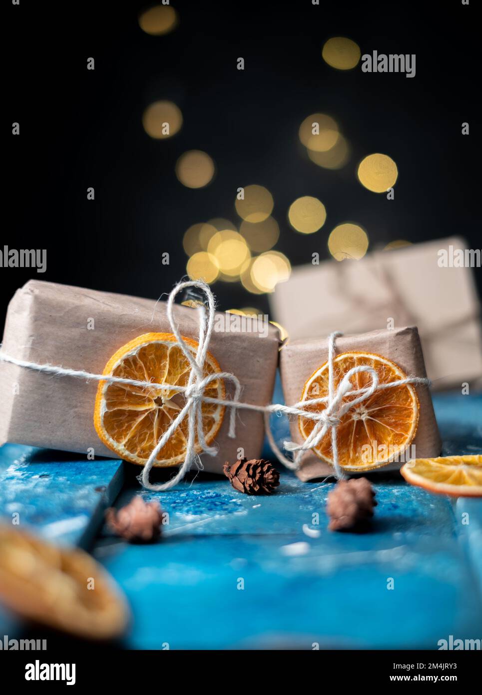 Umweltfreundliches Kraftpapier Geschenkpapier mit getrockneten Orangenscheiben auf einem blauen Tisch. Heimwerkergeschenke, umweltfreundliche Einrichtung. Hochformat Stockfoto