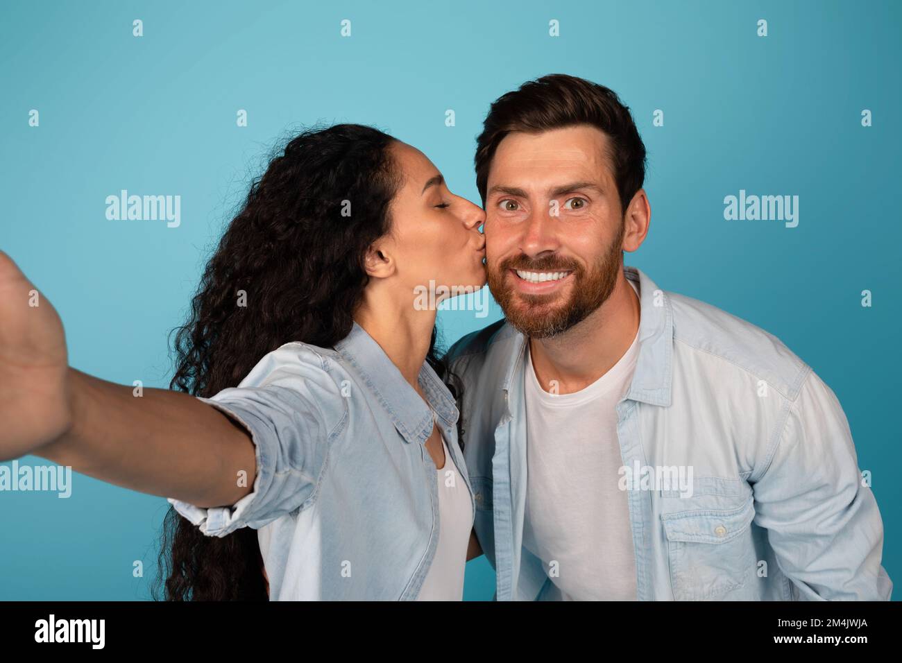 Lächelnde junge europäische Dame küsst männlich mit Bart und macht Selfie, genießt zärtliche Momente Stockfoto