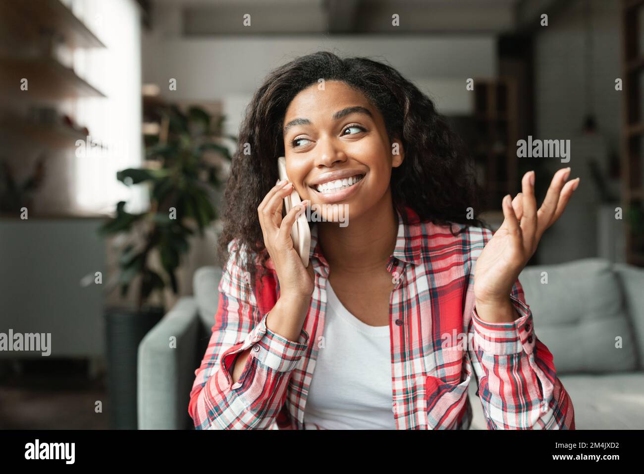 Eine glückliche, hübsche Millenial Black Lady ruft per Smartphone an, spricht mit einem Freund im Wohnzimmer, Nahaufnahme Stockfoto