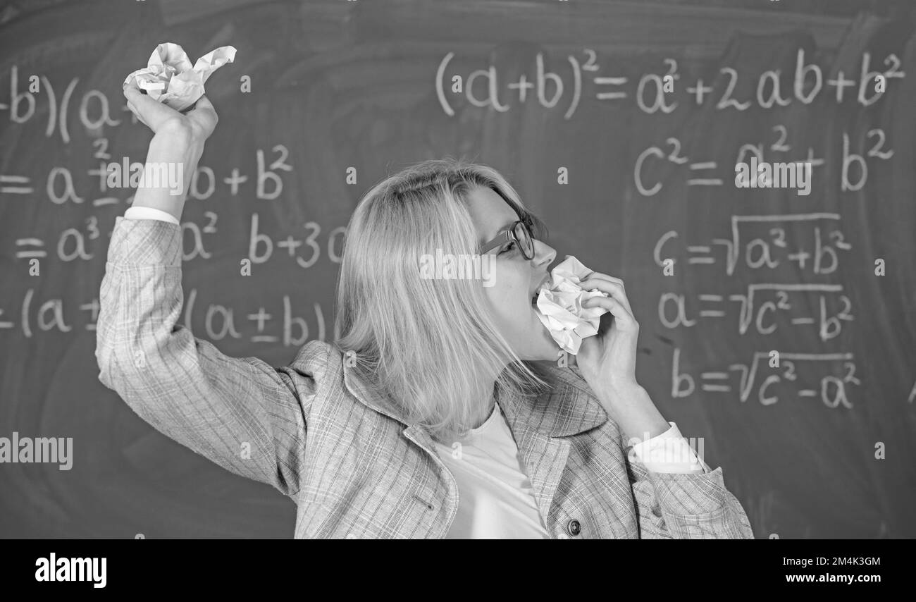 Der Lehrer isst ein Stück Papier und nimmt Informationen auf. Die Lehrerin ist bereit, ihren Papierkram zu essen. Lehrerin isst zerbrochenes Stück Papier mit Kreidetafelhintergrund Stockfoto