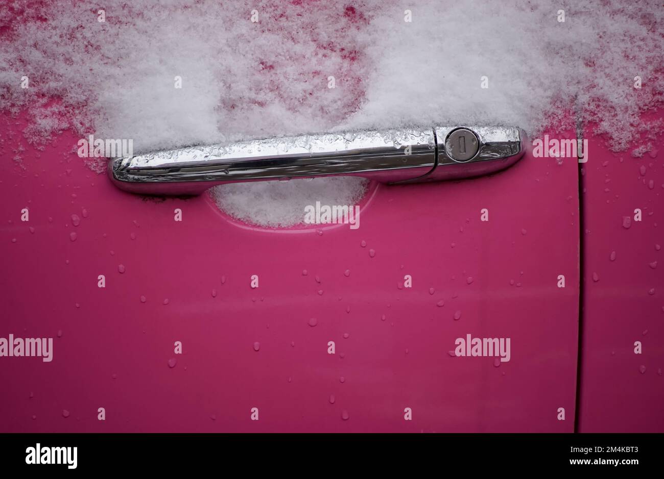 Der rosa Türgriff eines gefrorenen, verschneiten Autos. Stockfoto