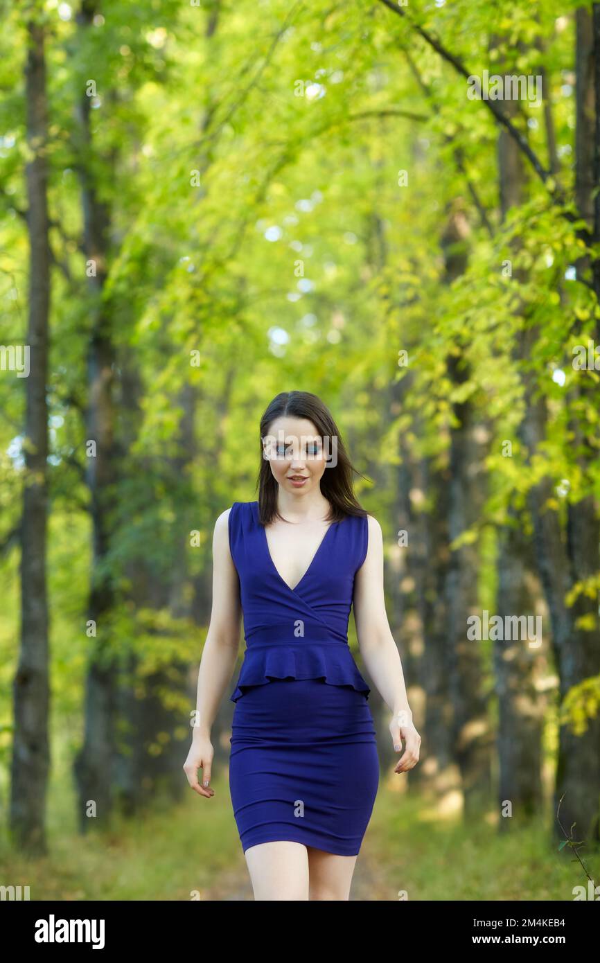 Eine Frau in blauem Kleid, die im Herbst auf einer Lindenallee spaziert. Pfad unter gelben Bäumen mit herbstlichen Blättern. Sonniger Herbsttag. Die Sonnenstrahlen Stockfoto