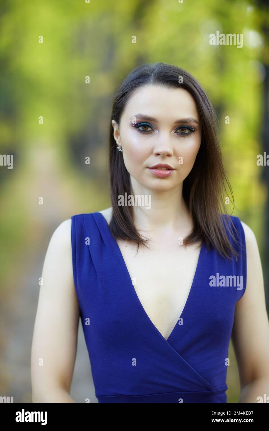Eine Frau in blauem Kleid, die im Herbst auf einer Lindenallee spaziert. Pfad unter gelben Bäumen mit herbstlichen Blättern. Sonniger Herbsttag. Die Sonnenstrahlen Stockfoto