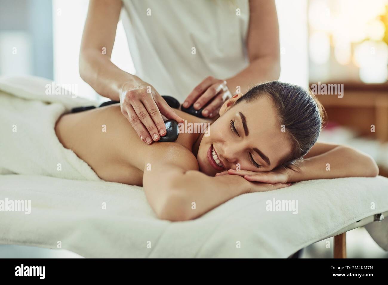 Die beruhigende Wirkung heißer Steine wird begrüßt. Eine attraktive junge Frau, die eine Hot-Stone-Massage in einem Schönheitssalon bekommt. Stockfoto