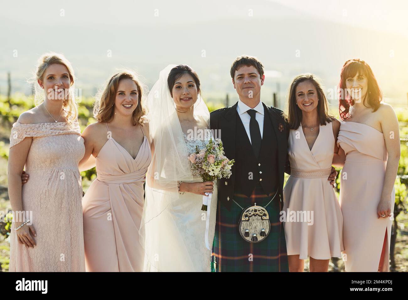 Was für ein stolzer Moment in unserem Leben. Porträt einer fröhlichen Braut und Bräutigam, die mit den Brautjungfern Arm in Arm draußen stehen. Stockfoto