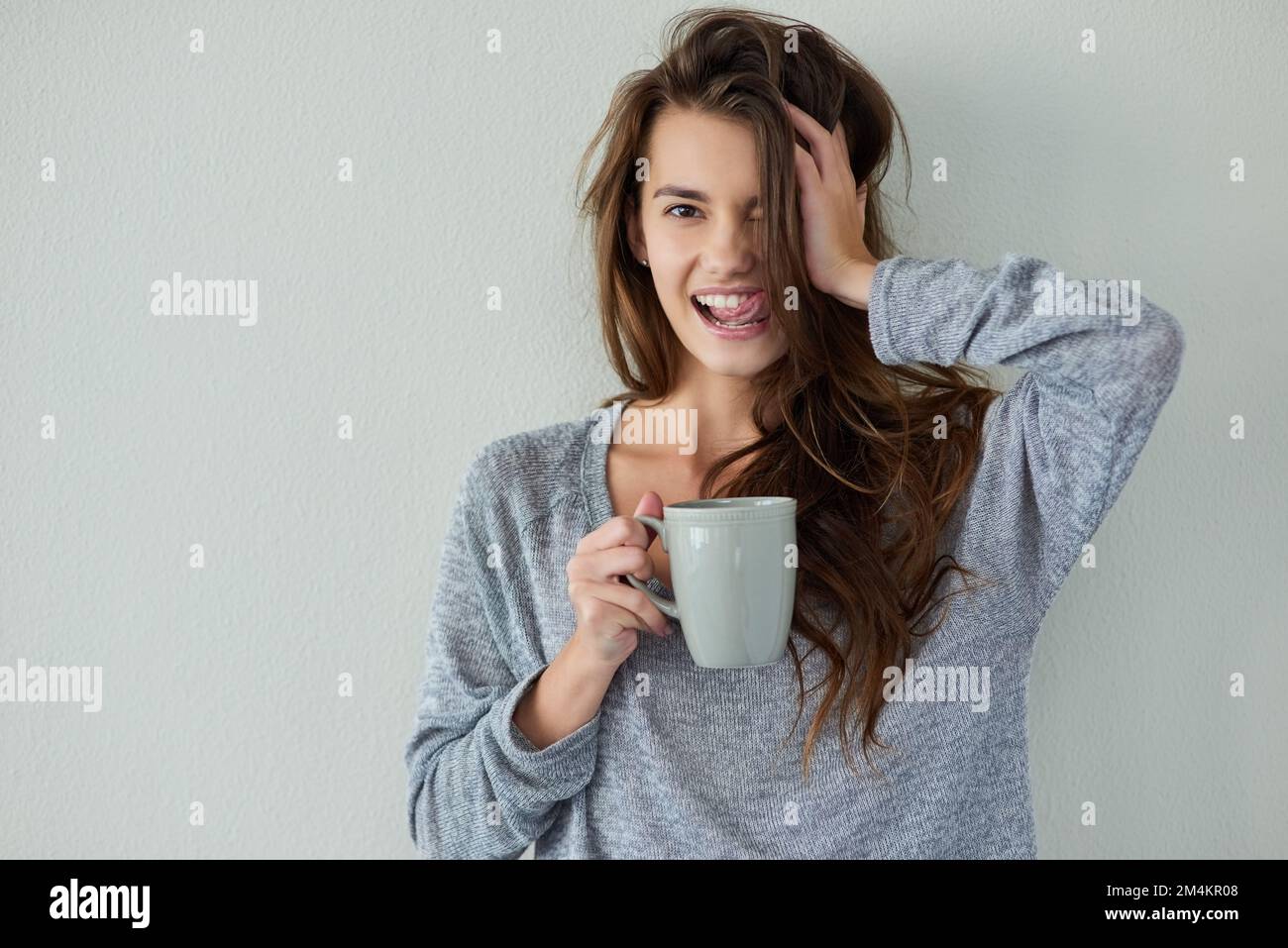 Was für ein langsamer Morgen. Studioaufnahme einer attraktiven jungen Frau, die die Seite ihres Kopfes hält, während sie Kaffee trinkt, vor weißem Hintergrund. Stockfoto