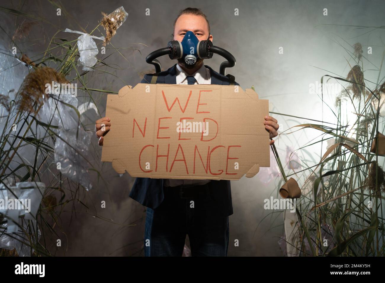 Ein Mann in einer Gasmaske in einem Anzug, umhüllt von Rauch, läuft in einer gefährlichen radioaktiven Zone mit einem Poster Wir brauchen Veränderung. Eine Plastikkatastrophe. Nach Apo Stockfoto