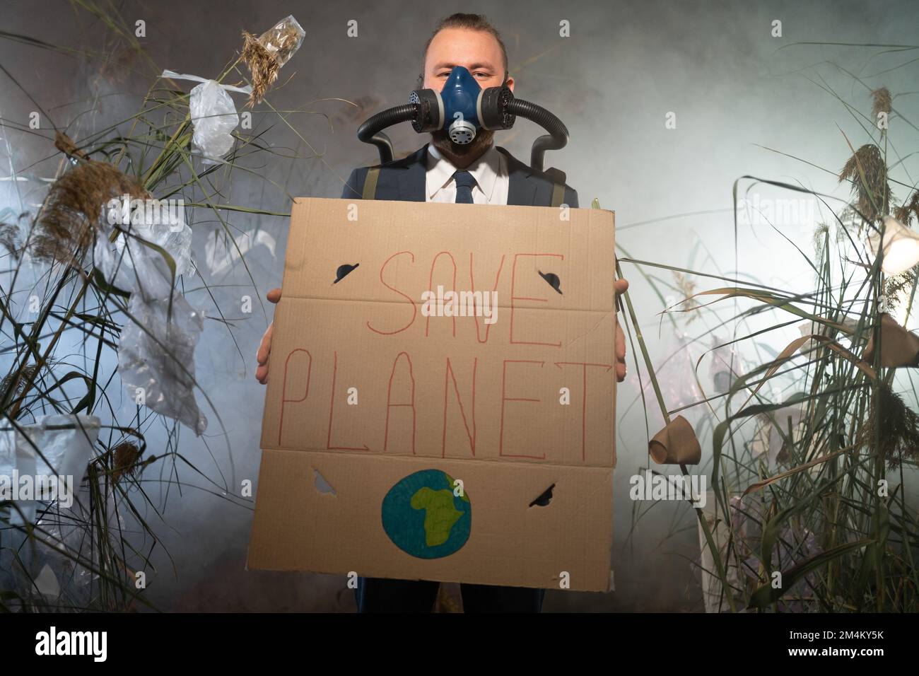 Ein Mann in einer Gasmaske in einem Anzug, umhüllt von Rauch, läuft in einer gefährlichen radioaktiven Zone mit Poster Save Planet. Eine Plastikkatastrophe. Post-Apocalyp Stockfoto