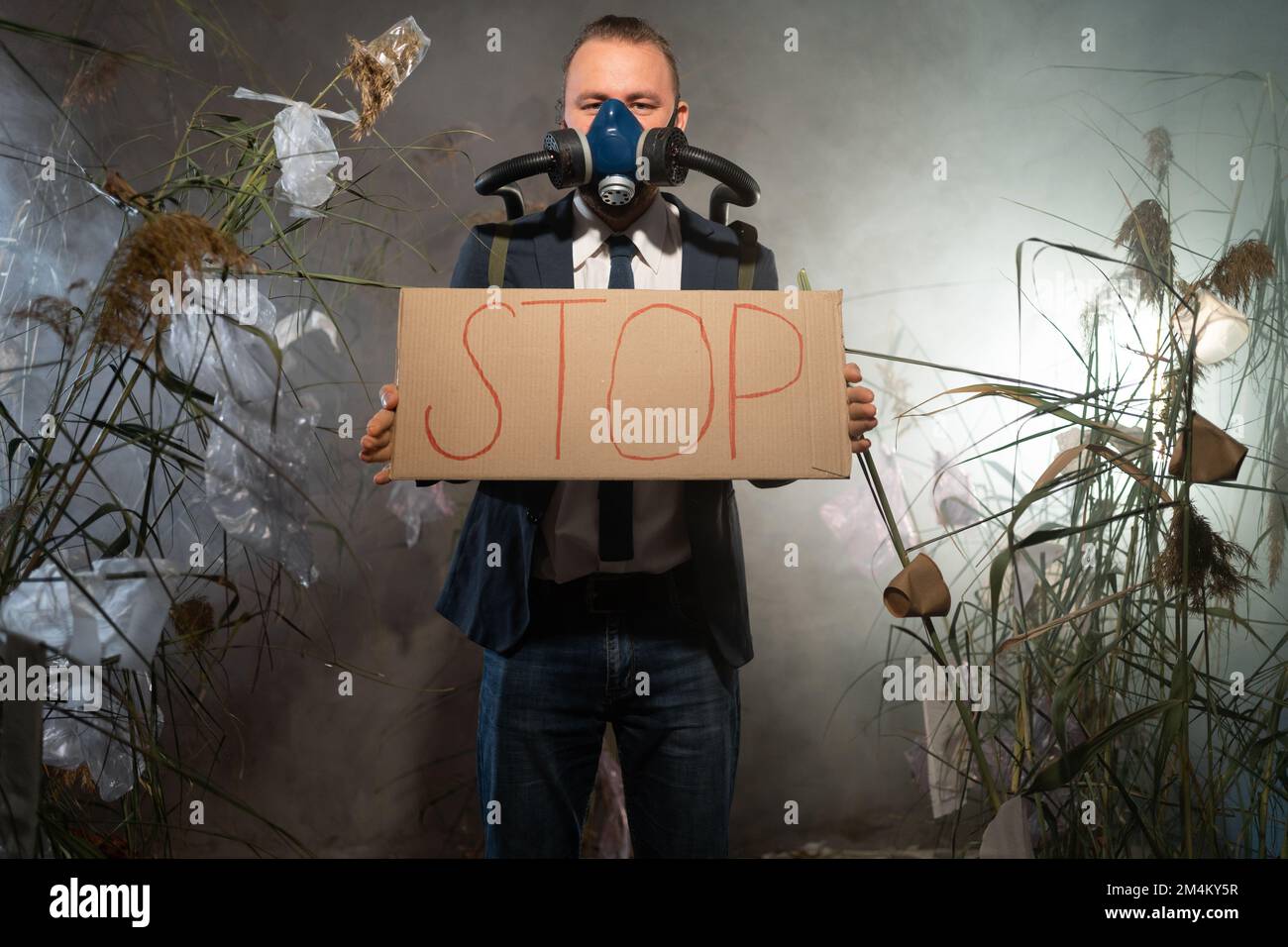 Ein Mann in einer Gasmaske in einem Anzug, der in Rauch umhüllt ist, läuft in einer gefährlichen radioaktiven Zone mit einem Poster Stop. Eine Plastikkatastrophe. Post-Apokalypse. E Stockfoto