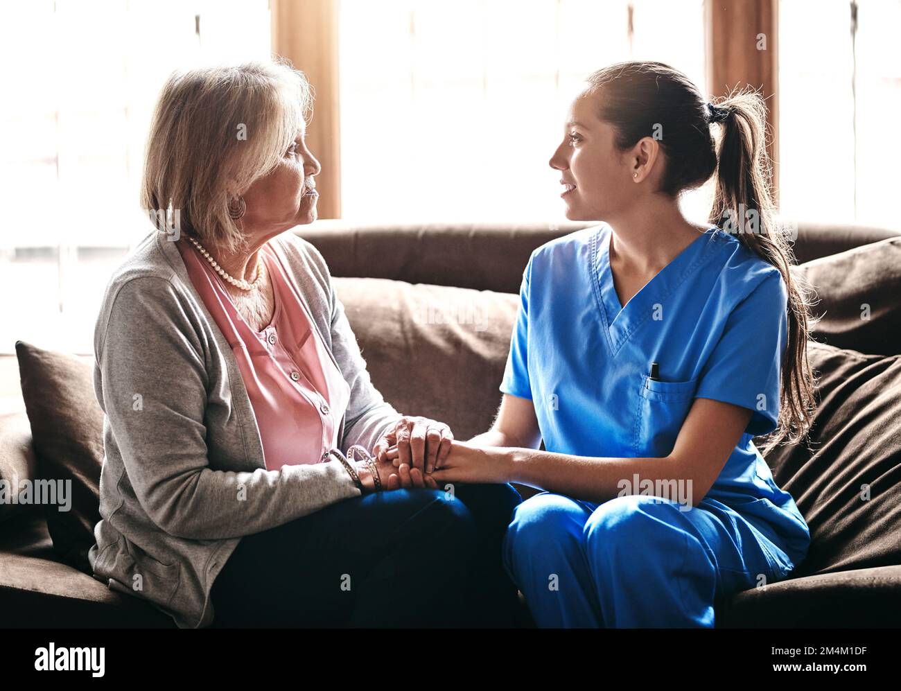 Sie haben eine besondere Verbindung: Eine Krankenschwester, die eine ältere Frau bequem die Hände hält. Stockfoto