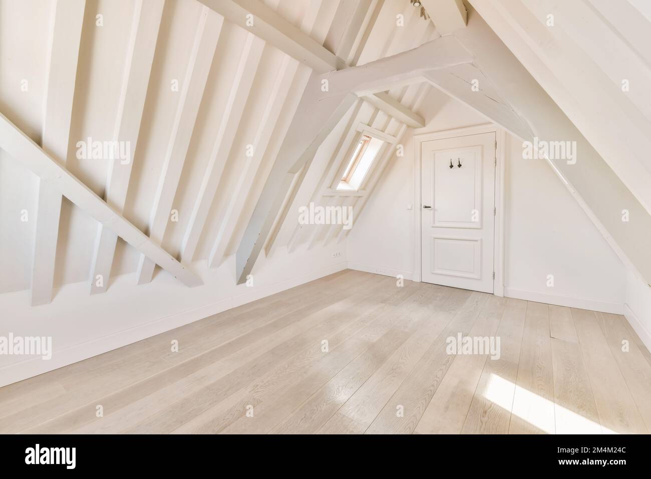 Ein Dachgeschoss-Zimmer mit weißen Wänden und Holzfußboden an der Wand, es gibt eine Tür in der Ecke Stockfoto