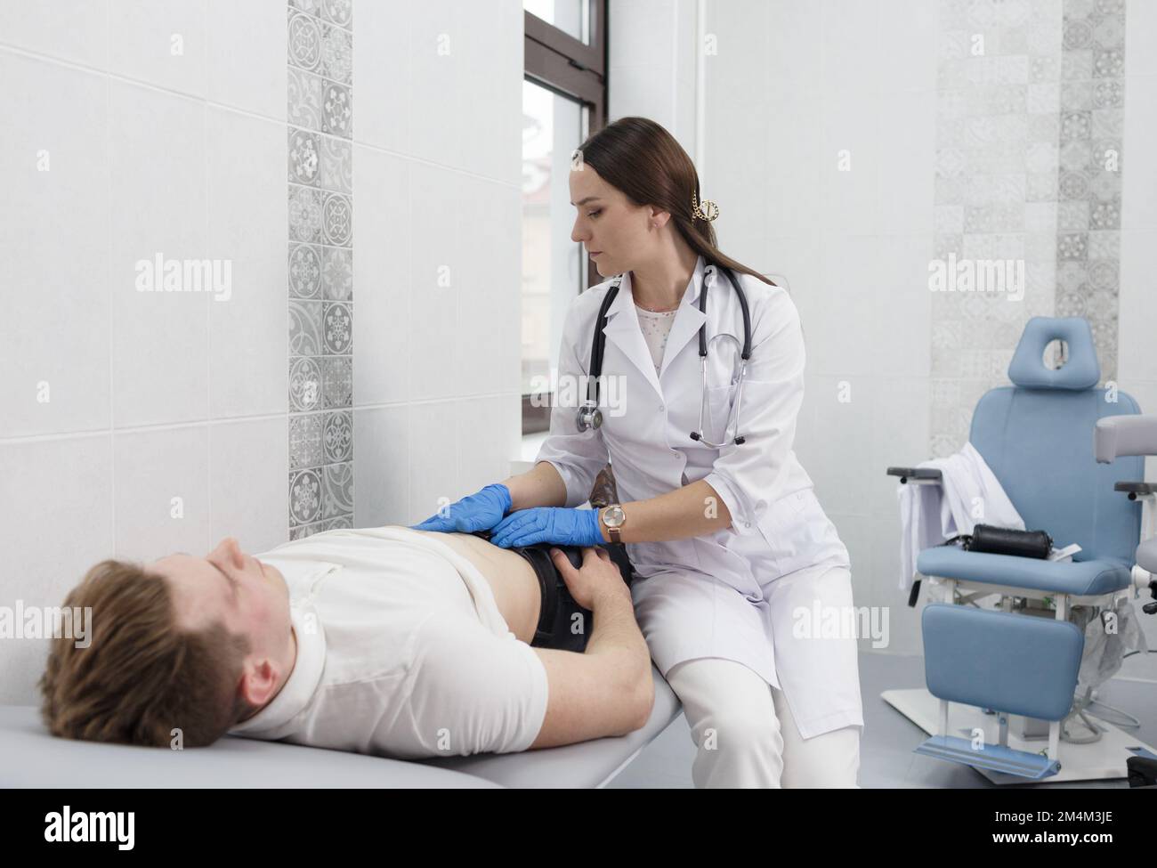 Eine fokussierte, junge Ärztin mit abdominaler Palpation bei einem schmerzhaften jungen Mann mittleren Alters. Stockfoto