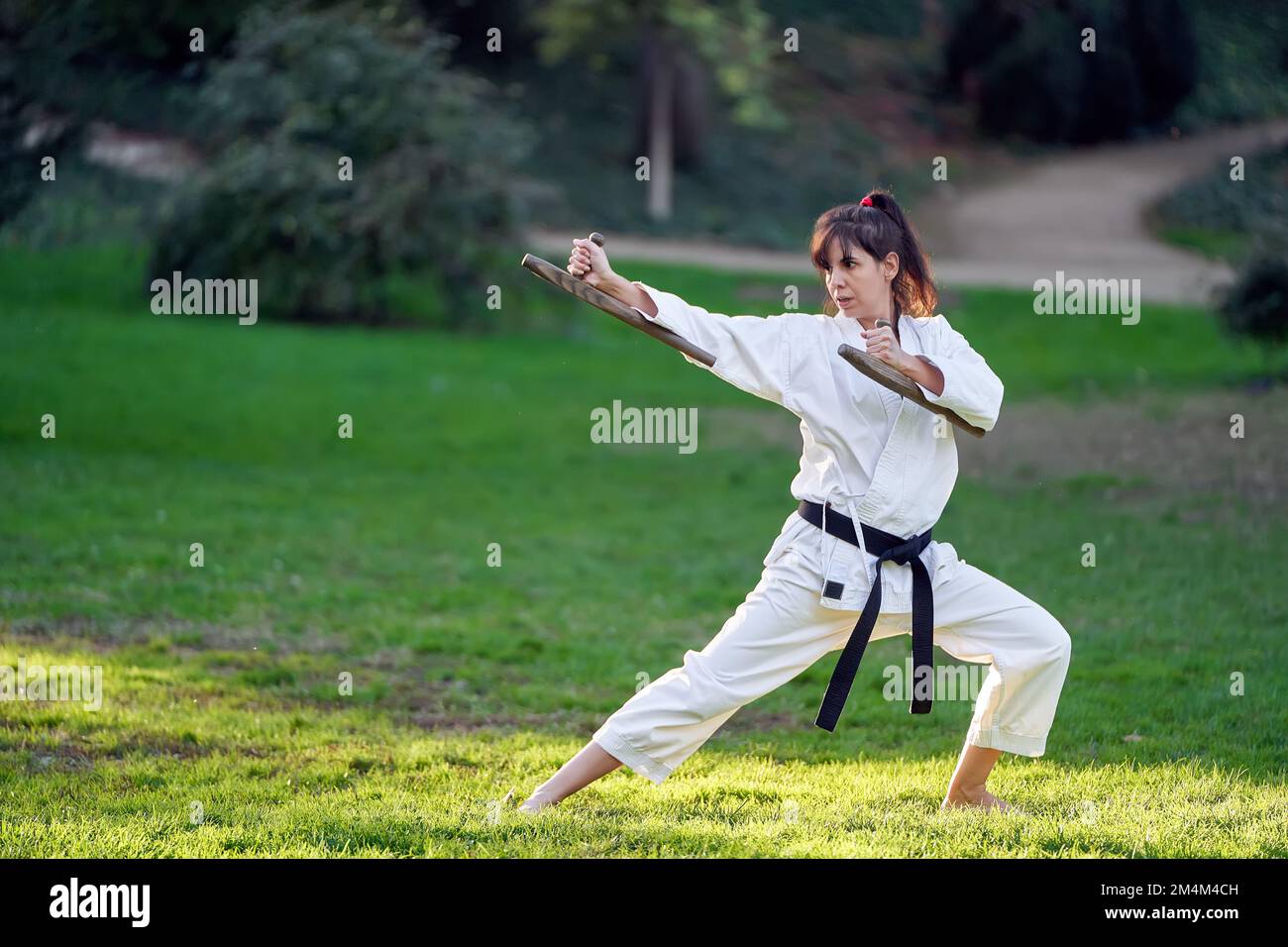Karate-Kämpferin in Kimono und schwarzer Gürtel, die beim Training im Freien in Karate-Pose steht. Sport- und Kampfsportkonzept. Stockfoto