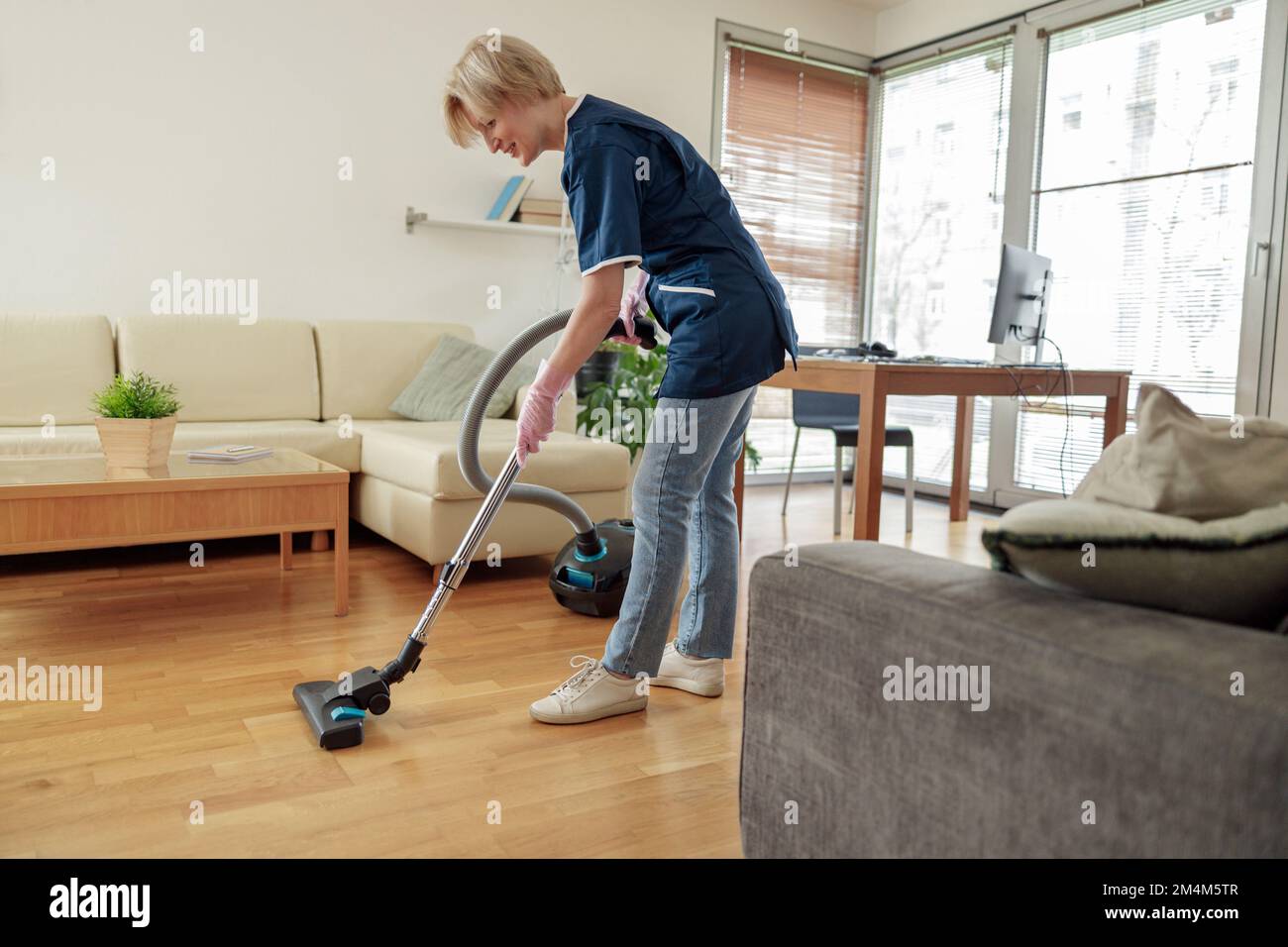 Professionelle Putzfrau trägt Uniform und saugt den Boden im Wohnzimmer Stockfoto