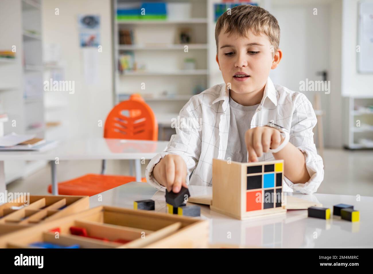 Glücklicher Junge, der Montessori-Stoff-Trinomialwürfel am Klassenschreibtisch zusammenstellt Stockfoto