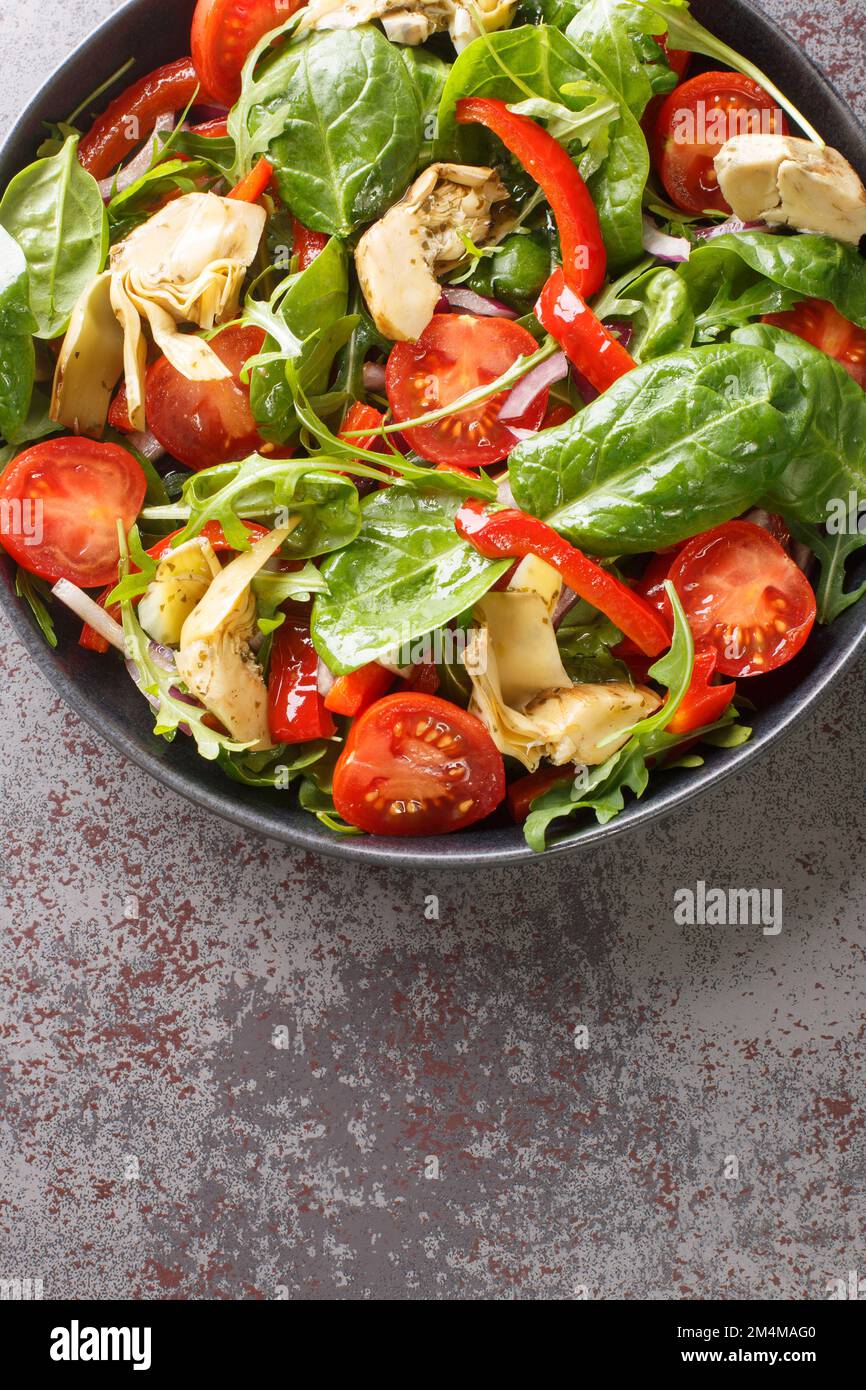 Diätetischer Salat mit eingelegten Artischocken, Tomaten, Spinat, Rucola, gebratenen Paprika und Zwiebeln in Nahaufnahme auf einem Teller auf dem Tisch. Vertikale Draufsicht von abo Stockfoto