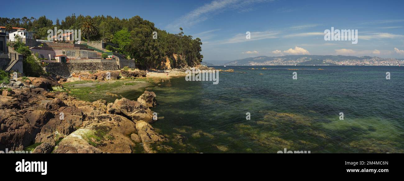 Panoramablick auf einen kleinen Strand zwischen Cangas und Moaña. Transparentes grünes Wasser mit Vigo City im Hintergrund Stockfoto