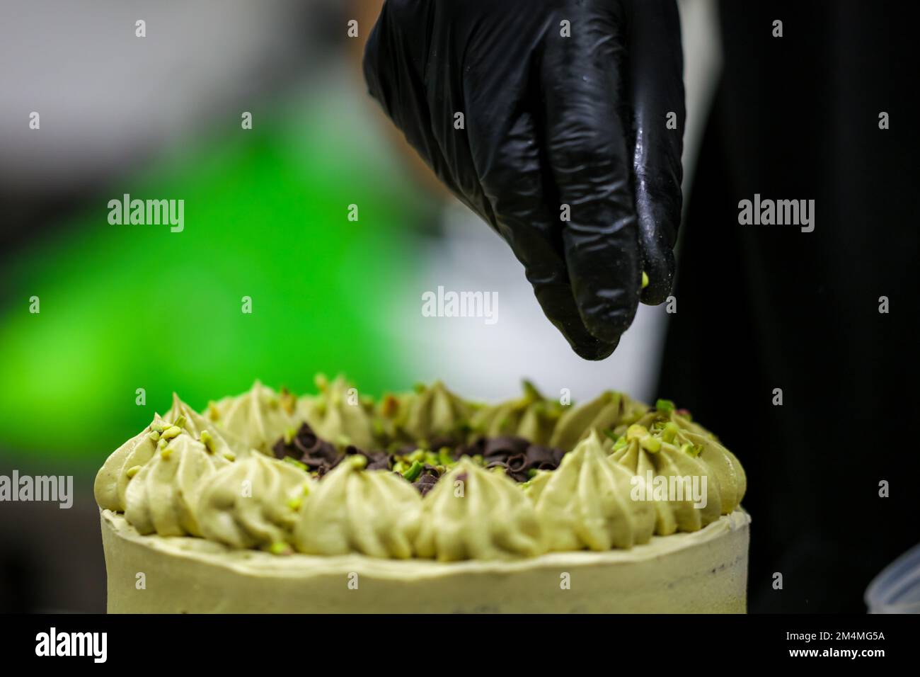 Der Konditoreidesigner streut den grünen, mattierten Schokoladenkuchen mit kleinen pistacchio- und dunklen Schokoladenstücken Stockfoto