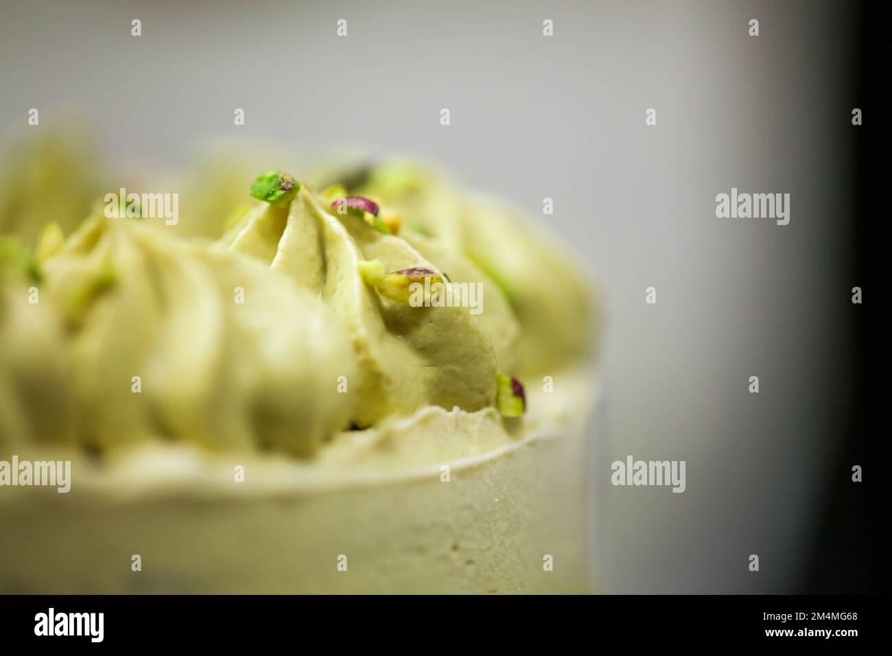 Der Konditoreidesigner streut den grünen, mattierten Schokoladenkuchen mit kleinen pistacchio- und dunklen Schokoladenstücken Stockfoto
