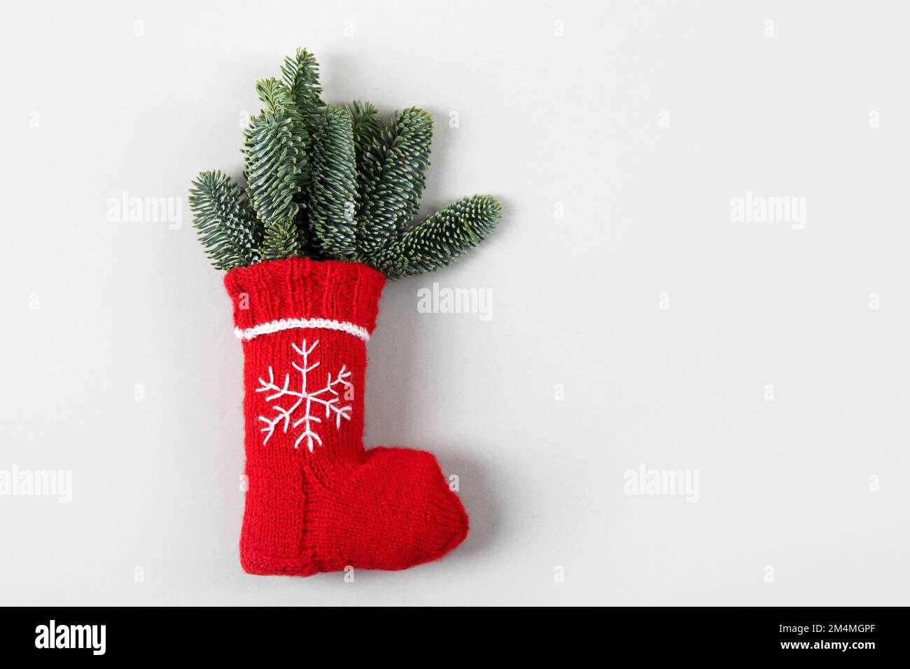 Rote Weihnachtssocke mit einer gestickten weißen Schneeflocke und grünen Zweigen eines Weihnachtsbaums auf grauem Hintergrund mit einer Textstelle. Stockfoto