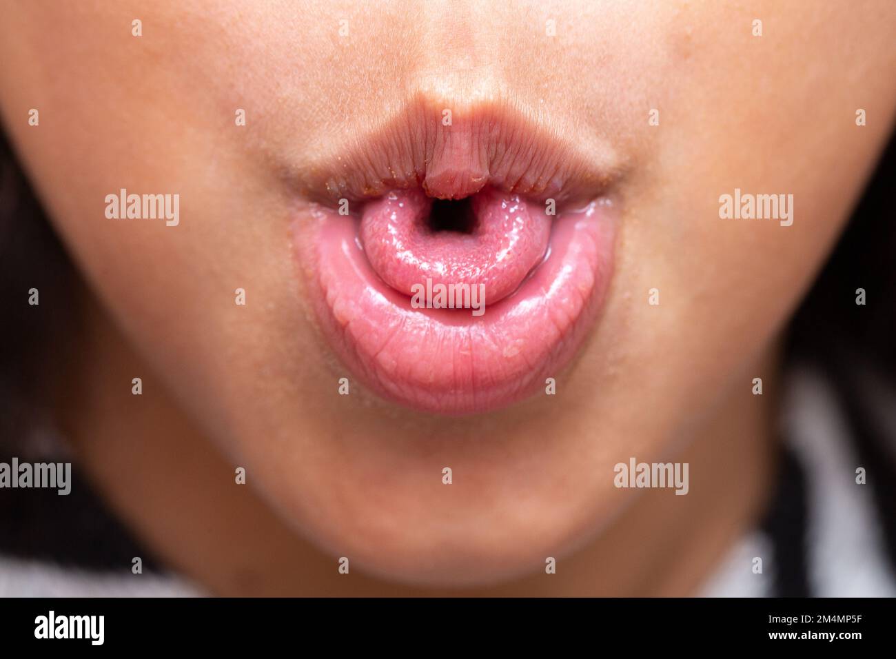 Makro eines kleinen Mädchens Mund, der seine Zunge in U-Form lockt, ein genetisches Merkmal, das von ihren Eltern geerbt wurde. Stockfoto