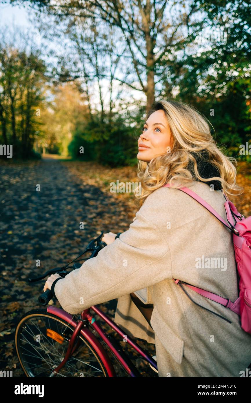 Junge attraktive weiße Frau fährt im Herbst an warmen Tagen mit dem Fahrrad im Park. Stockfoto