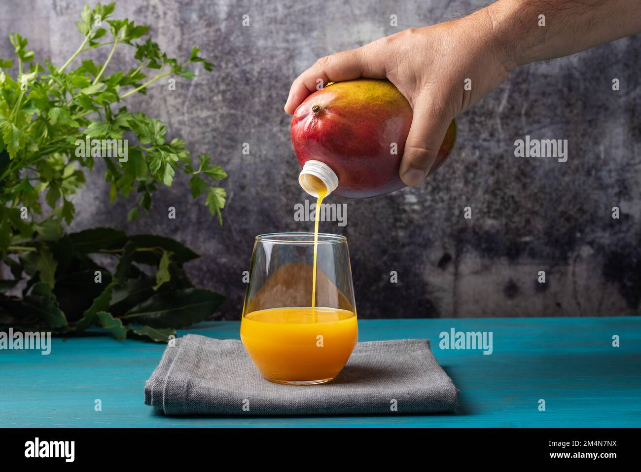 Die Hand hält eine Frucht, Mango, die einen Ausguss hat, durch den sie den Saft in das Glas gießt, als wäre es eine Flasche. Stockfoto