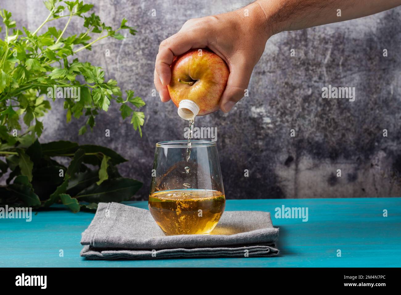 Die Hand hält ein Obst, einen Apfel, durch den sie den Saft in das Glas gießt, als wäre es eine Flasche. Stockfoto