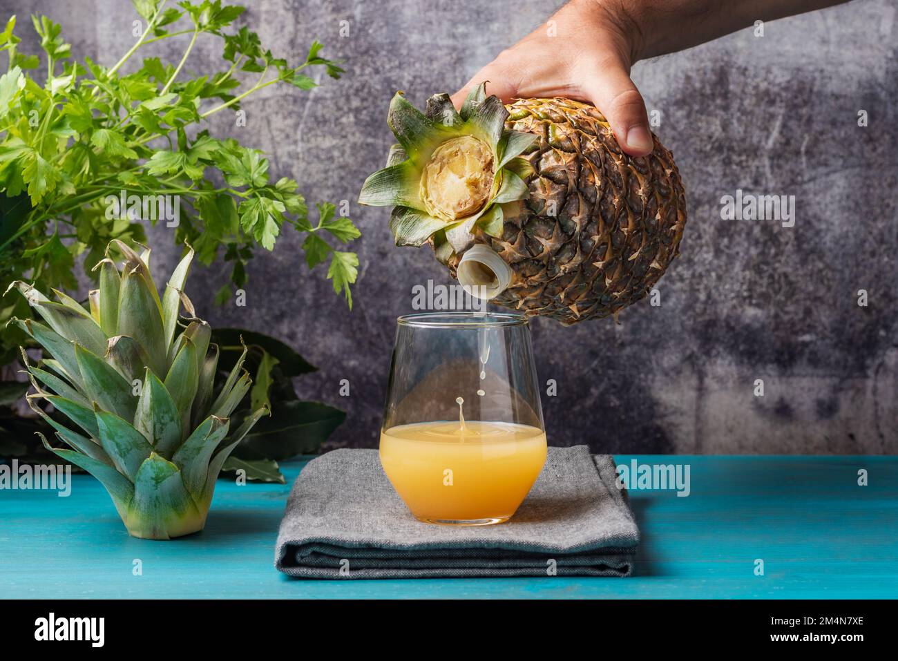 Die Hand hält eine Frucht, Ananas, die einen Ausguss hat, durch den sie den Saft in das Glas gießt, als wäre es eine Flasche. Stockfoto