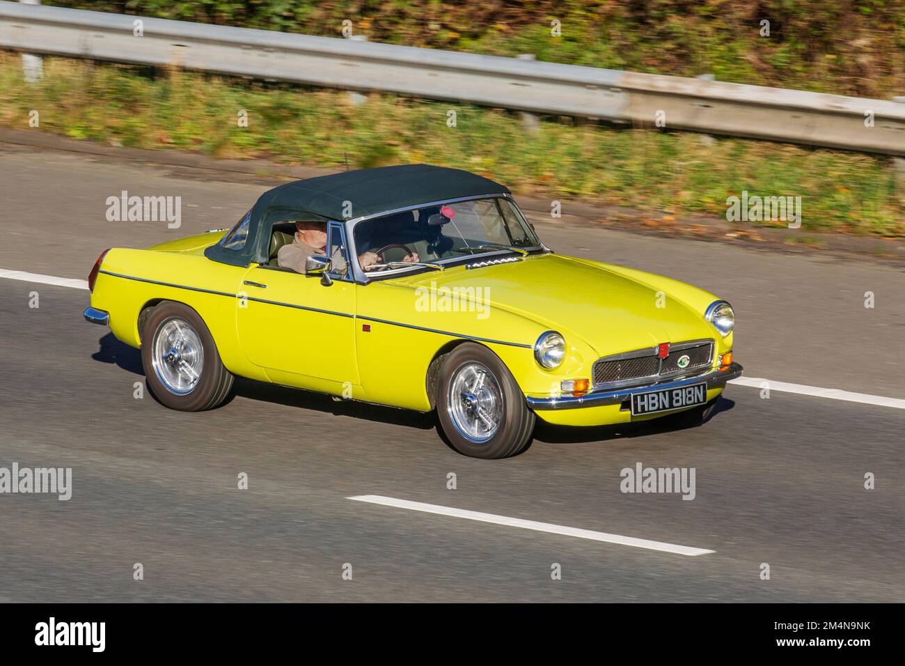 1975 70s, 70er Yellow MG B MGB, ein zweitüriger Sportwagen, der von 1962 bis 1980 von der British Motor Corporation (BMC) 1798cc Petrol British Sports Cabrio hergestellt und vermarktet wird und auf der Autobahn M6 in Großbritannien fährt Stockfoto