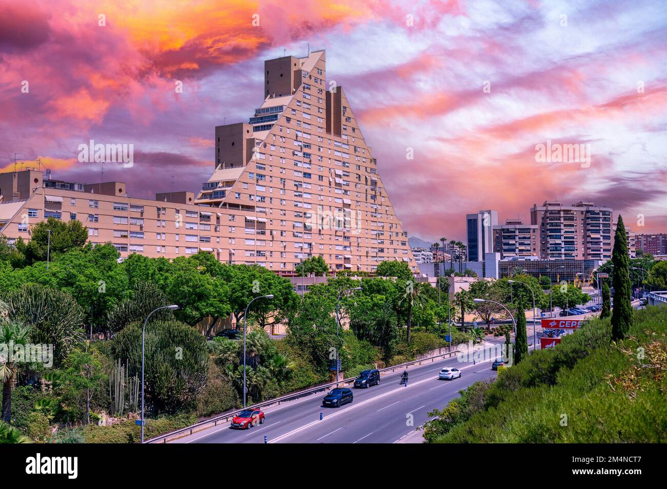 Ein Apartmentgebäude mit ungewöhnlicher Pyramidenform steht an einer geschäftigen Straße oder Straße in Alicante City. Stockfoto