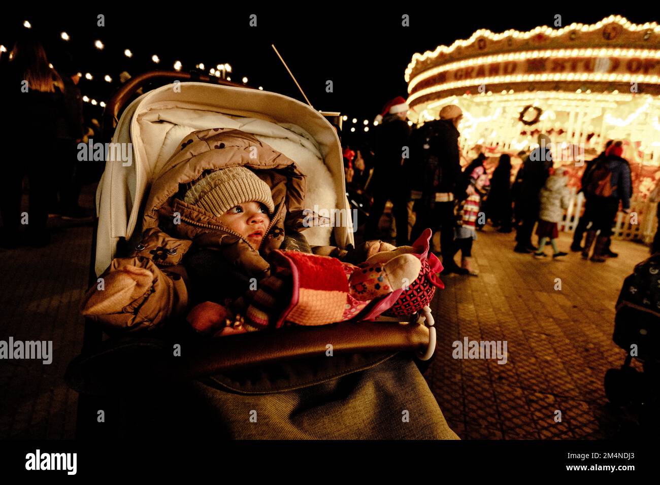 Ein Baby sieht auf einem Rummel zu, mit einem Riesenrad hinter ihr. Stockfoto