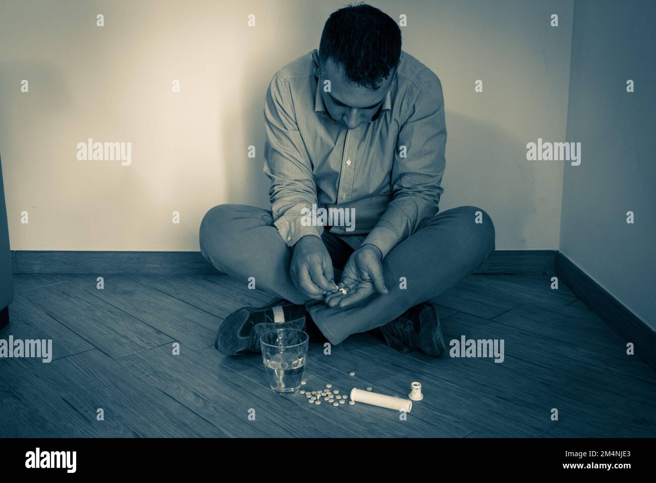 Bild eines verzweifelten Mannes, der auf dem Boden sitzt und Pillen missbraucht. Drogen- und Drogenmissbrauch und Suchtproblem. Stockfoto