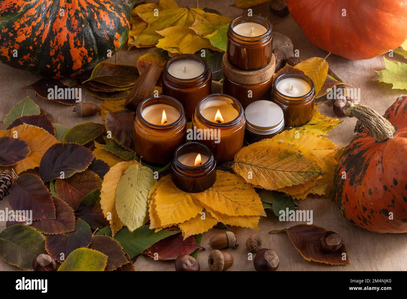 Sojalkerzen brennen in Gläsern. Baumblätter, Kürbis. Komfort zu Hause. Kerze in einem braunen Glas. Duft und Licht. Handgemachte Duftkerze. Aromatherapie. Herbststimmung. Gemütliches Wohndekor im Herbst. Stockfoto