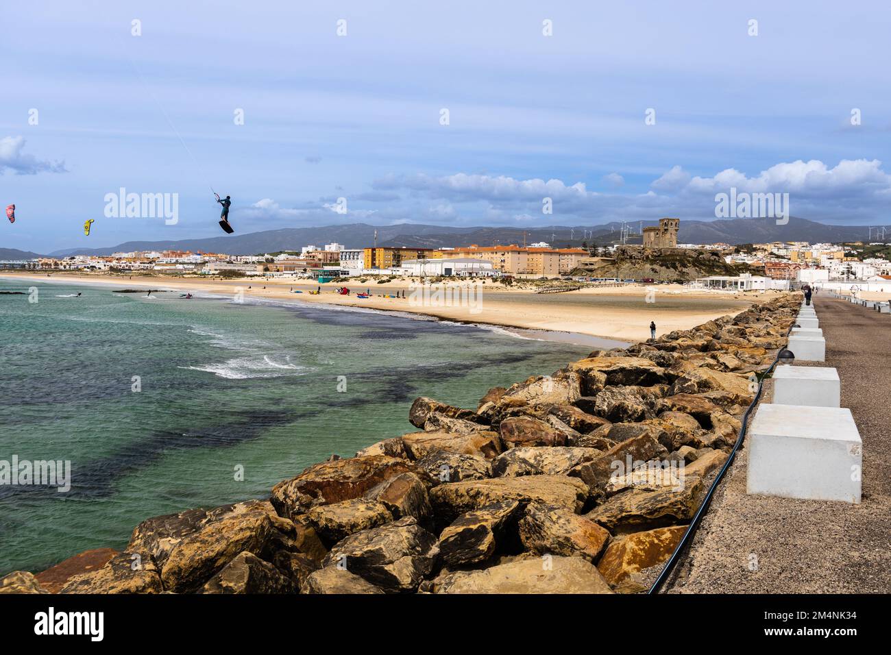 Kitesurfer fahren über das Meer in Strandnähe mit Tarifa Stadt im Hintergrund. Andalusien, Spanien. Sonniger und windiger Frühlingstag. Stockfoto