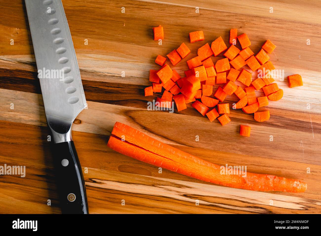 Gewürfelte Karotten auf einem Holzschneidbrett: Karotten schälen und mit einem Messer in kleine Würfel auf einem Schneidebrett schneiden Stockfoto