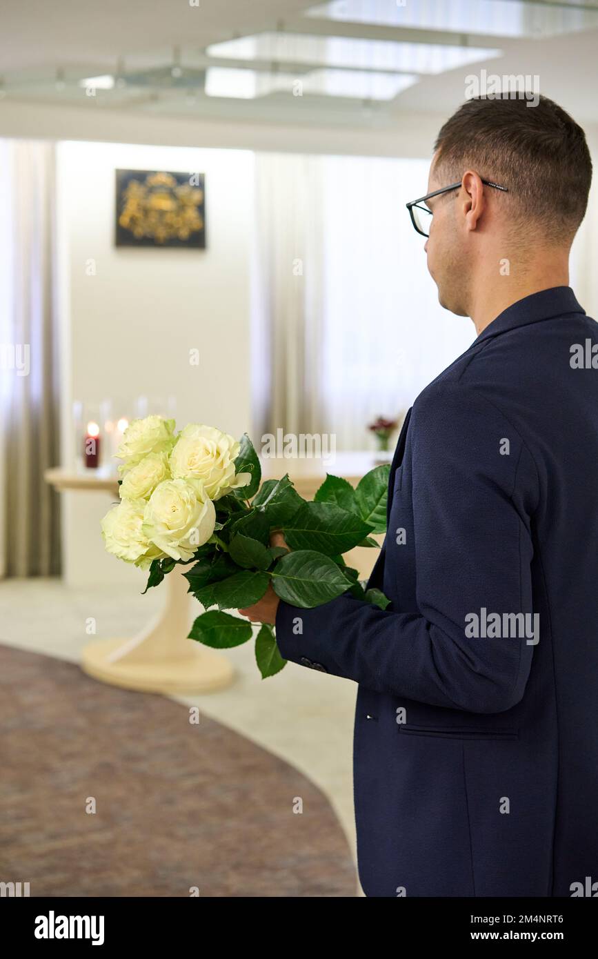 Olaine, Lettland - 17. November 2022: Ein Mann in dunkler Jacke hält einen frischen weißen Rosenstrauß. Blick von hinten. Festungskonzept. Stockfoto