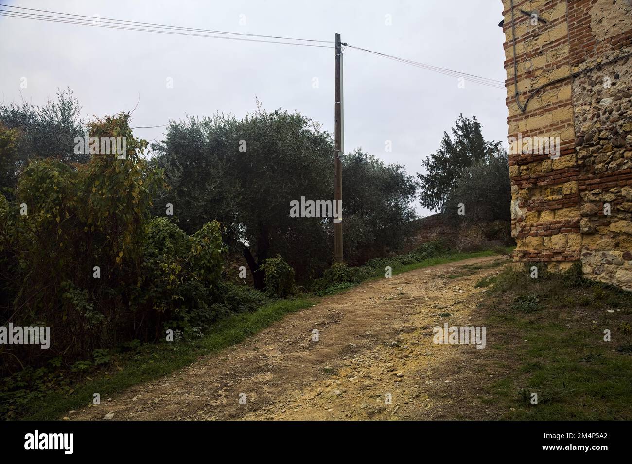 Ecke einer Festung neben einem schmutzigen Pfad und einem Olivenhain an einem bewölkten Tag Stockfoto