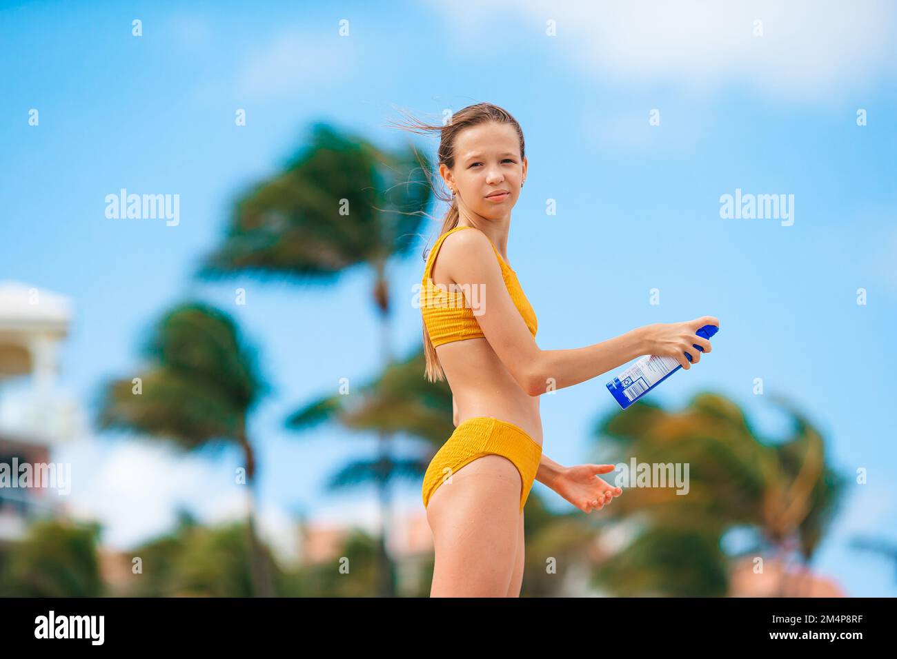 Ein bezauberndes Teenager-Mädchen in gelbem Bikini, das Sonnencreme am Strand aufträgt Stockfoto