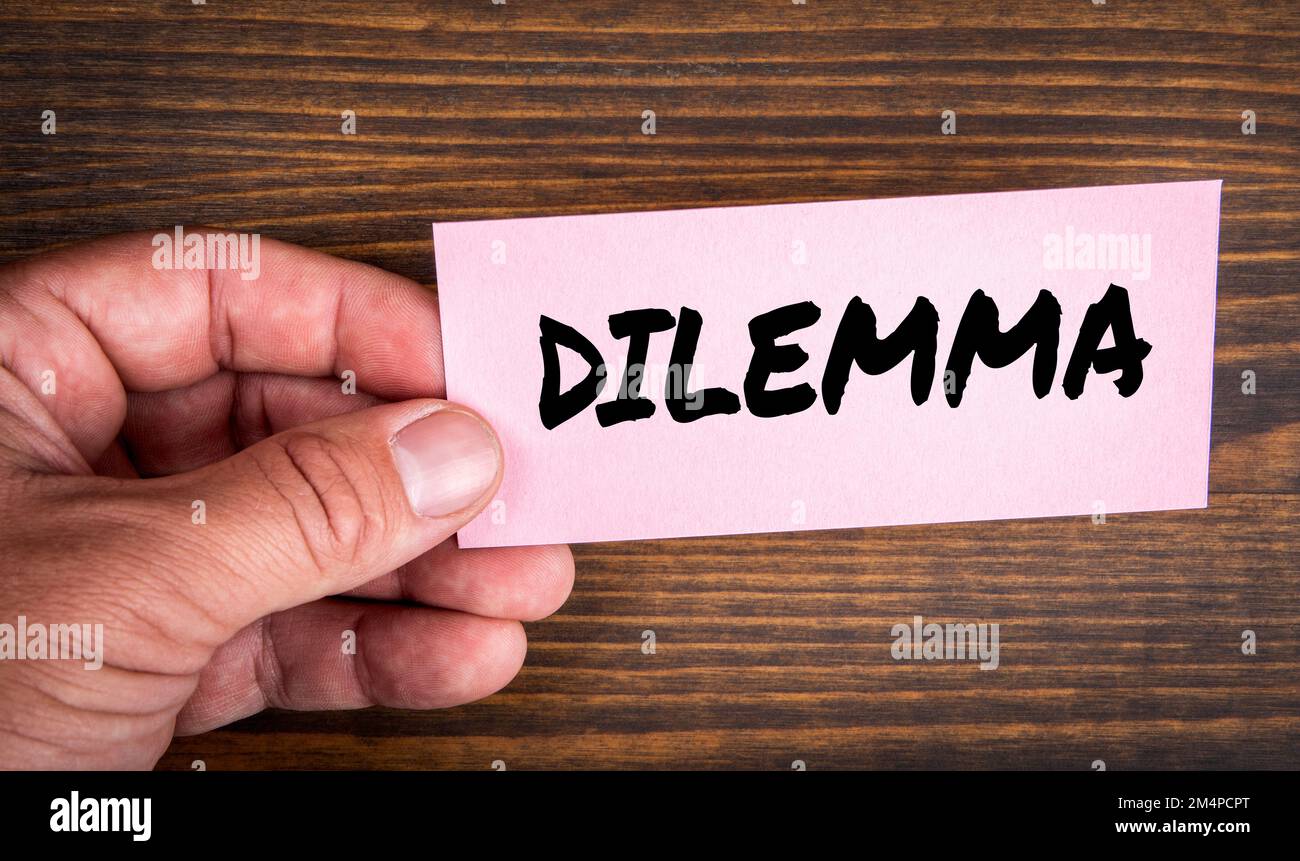 DILEMMA. Rosafarbenes Blatt Papier mit Text in der Hand auf einem holzstrukturierten Hintergrund. Stockfoto