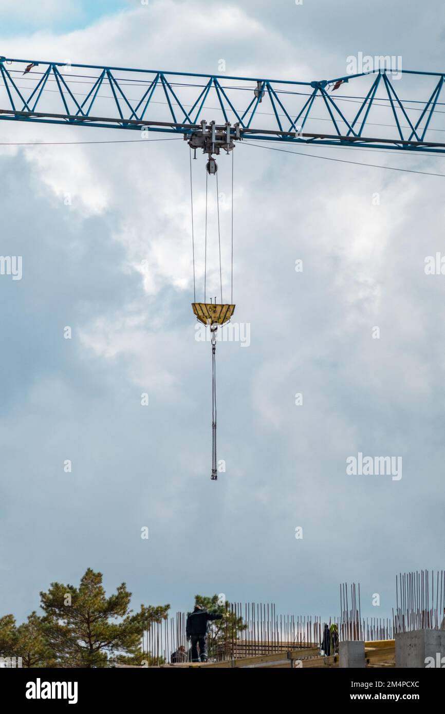 Blauer, hoher Kragarm zum Heben schwerer Gewichte auf der Baustelle eines mehrstöckigen Gebäudes mit bewölktem, landschaftlich schönen Himmelshintergrund Stockfoto