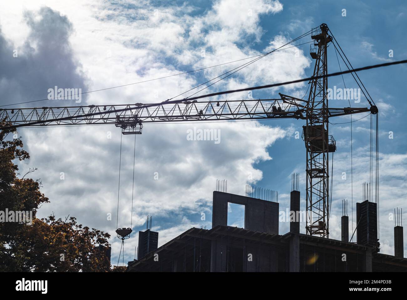 Hoher vorstehender Kranarm zum Heben schwerer Gewichte auf der Baustelle eines mehrstöckigen Gebäudes mit bewölktem, landschaftlich schönen Himmelshintergrund Stockfoto