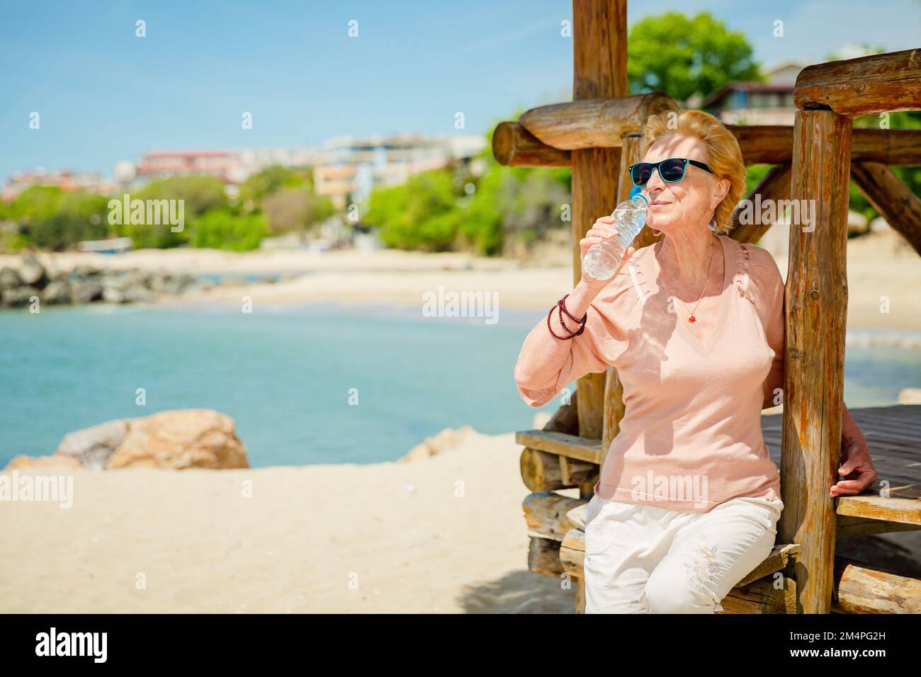 Ältere Frau, die mit einer Flasche Wasser am Strand sitzt Stockfoto